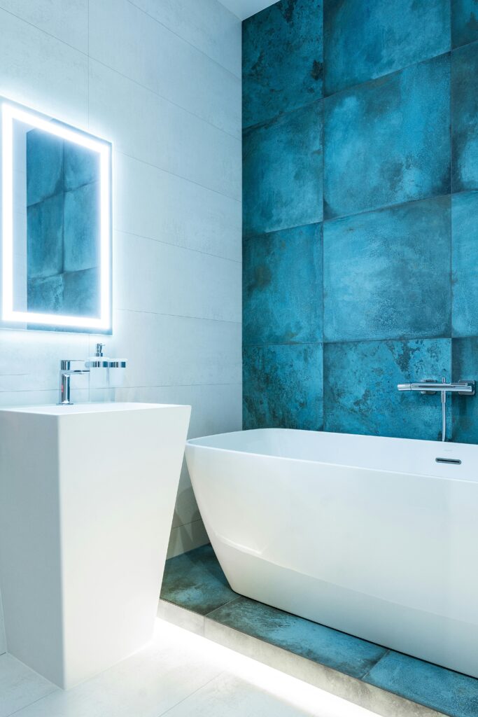 Stylish contemporary bathroom featuring a white bathtub and blue accent wall, illuminated by soft lighting.